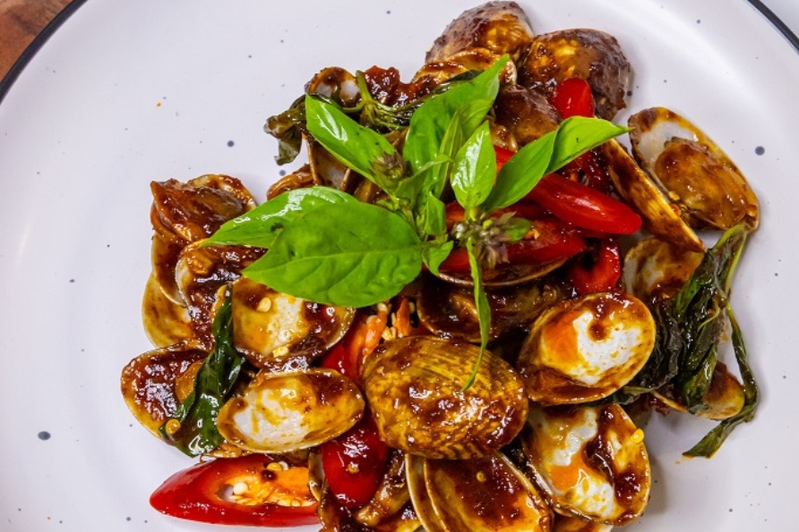 A plate of Spicy Stir-Fried Clams with Basil (ผัดหอยลาย), featuring fresh clams, vibrant red chillies, and aromatic Thai basil in a glossy, flavourful sauce.